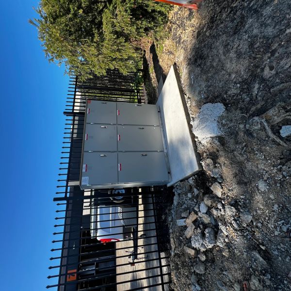 Outdoor electrical control panel mounted on a concrete slab near a fence.
