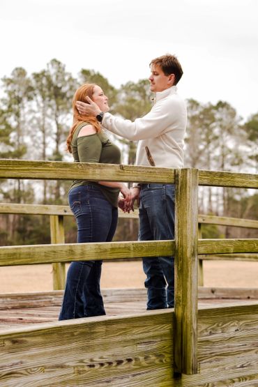 Couple holding hands and sharing a tender moment on a wooden bridge outdoors.