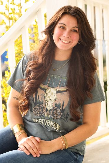 Smiling woman with long curly hair sitting outdoors in casual attire.