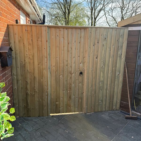 Wooden garden gate with a metal handle and broom nearby.