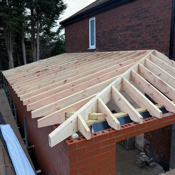Wooden roof frame construction on a brick structure under cloudy sky.