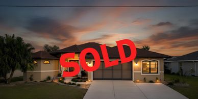 Modern house at sunset with a red SOLD sign.
