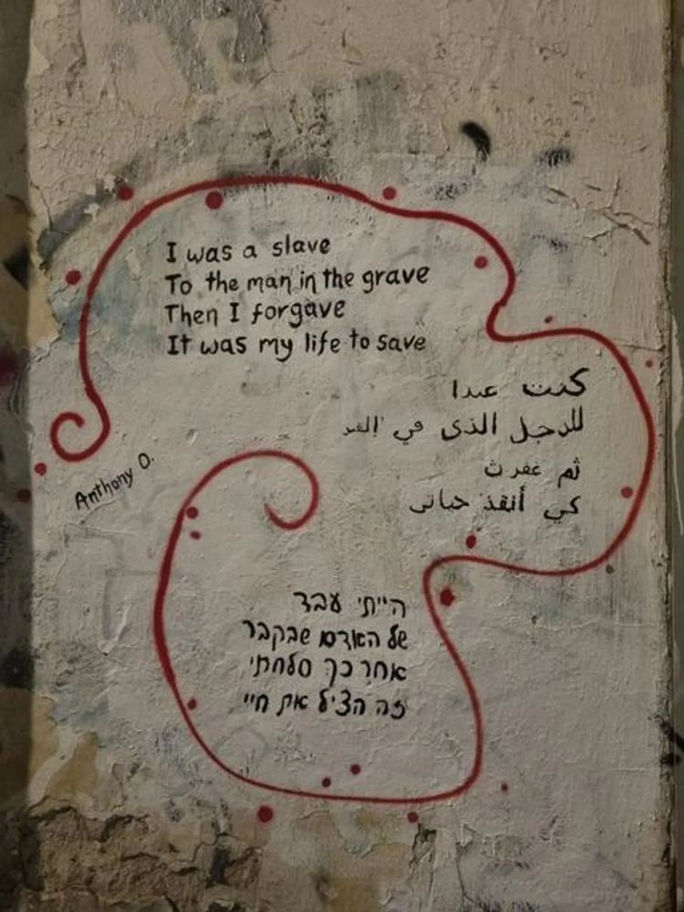Wall graffiti with a poetic message in English, Arabic, and Hebrew.
