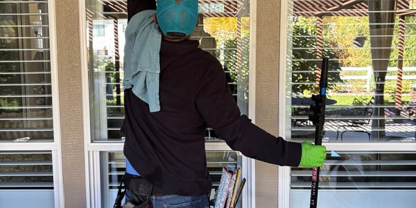 A worker cleaning a window with tools and gloves.