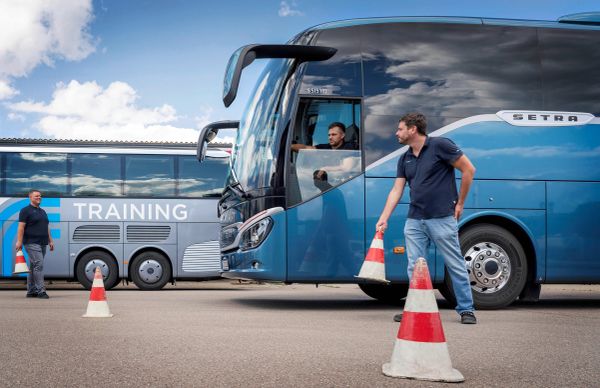 Men training to maneuver a bus with traffic cones.