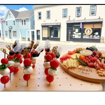 Skewered appetizers with cherry tomatoes, mozzarella, and basil in front of a wooden charcuterie board.