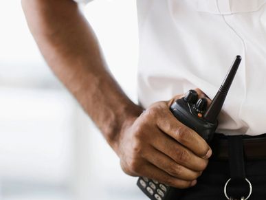 Security personnel holding a walkie-talkie attached to their belt.