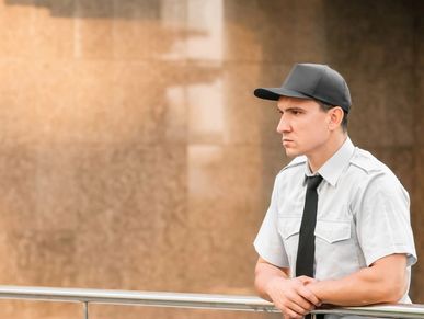 A serious security guard in uniform and cap standing by a railing.
