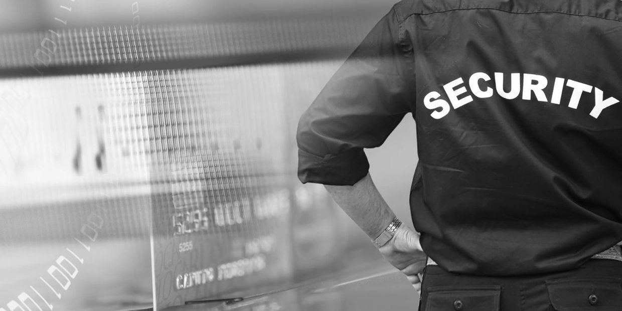 Security guard standing with hands on hips in front of a digital screen.
