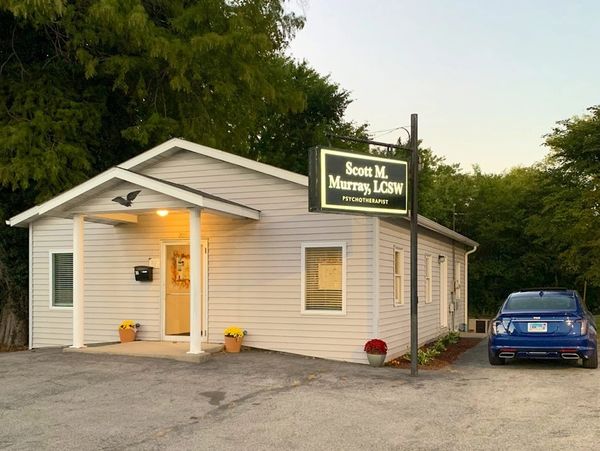 Cozy psychotherapy office in a small white building with a blue car parked outside.