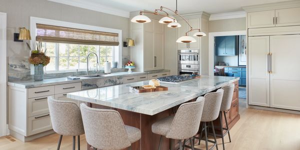 Modern kitchen with marble island and beige chairs.