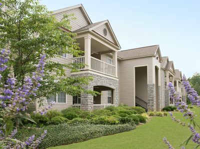 Modern apartment complex with stone accents and lush landscaping under clear blue sky.