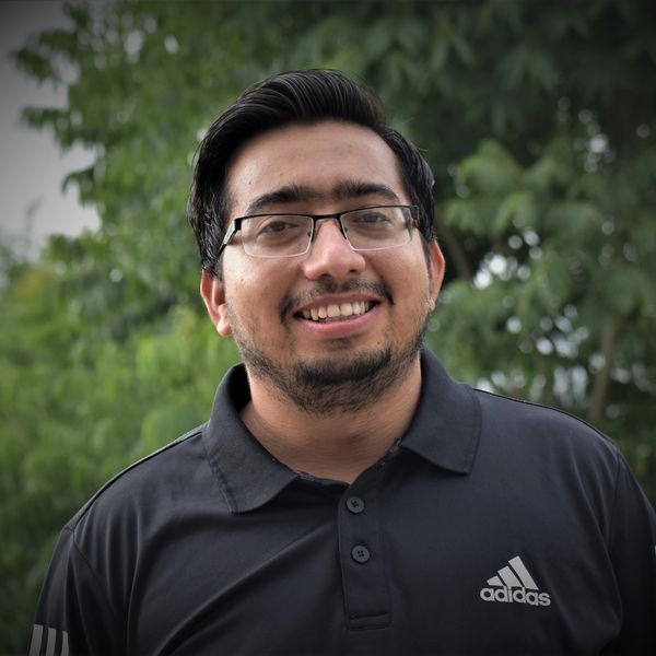 Smiling man wearing glasses and black Adidas polo outdoors.