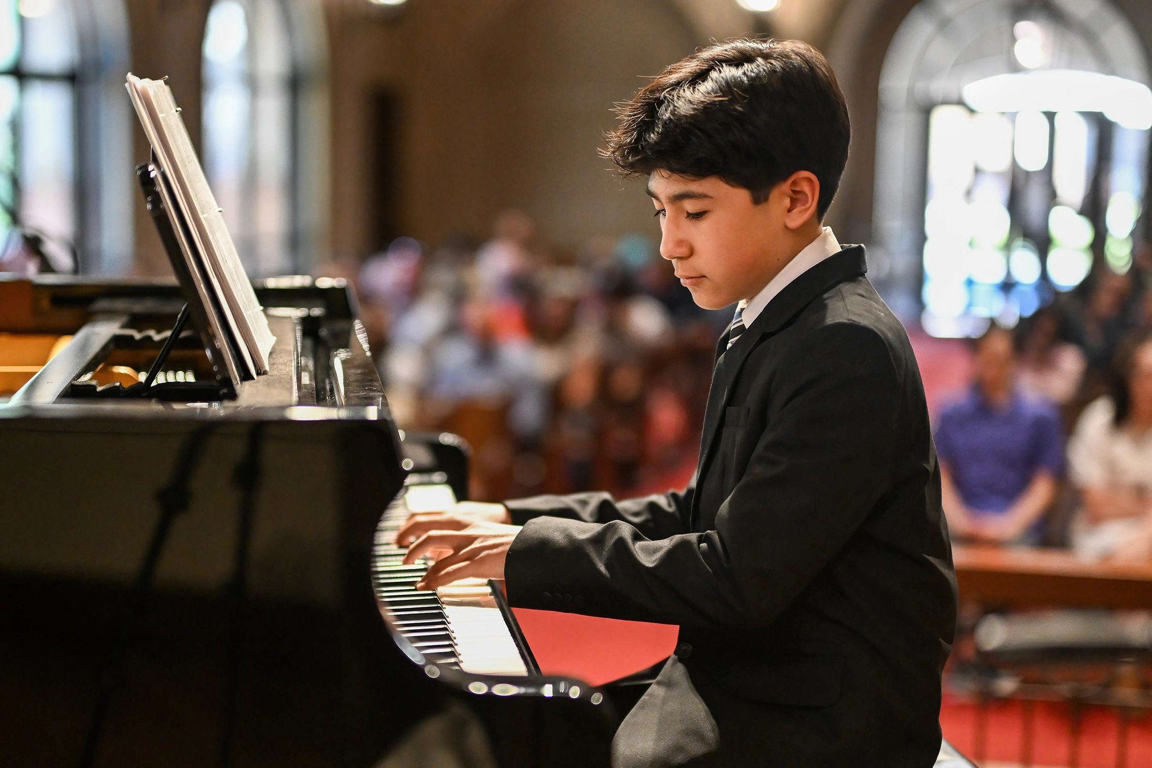 Young boy in a suit playing piano with focus in a formal setting.
