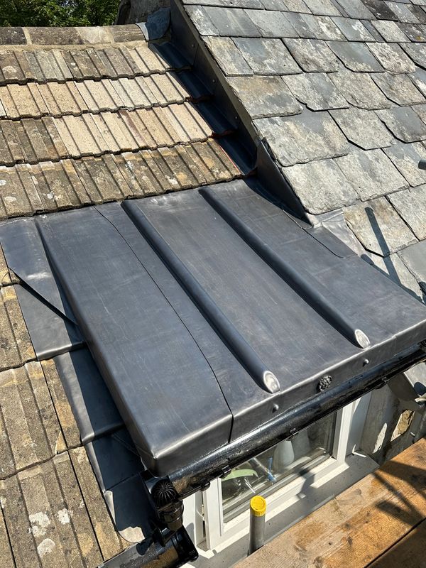 A roof section showing different types of tiles and a metal flashing around a window.