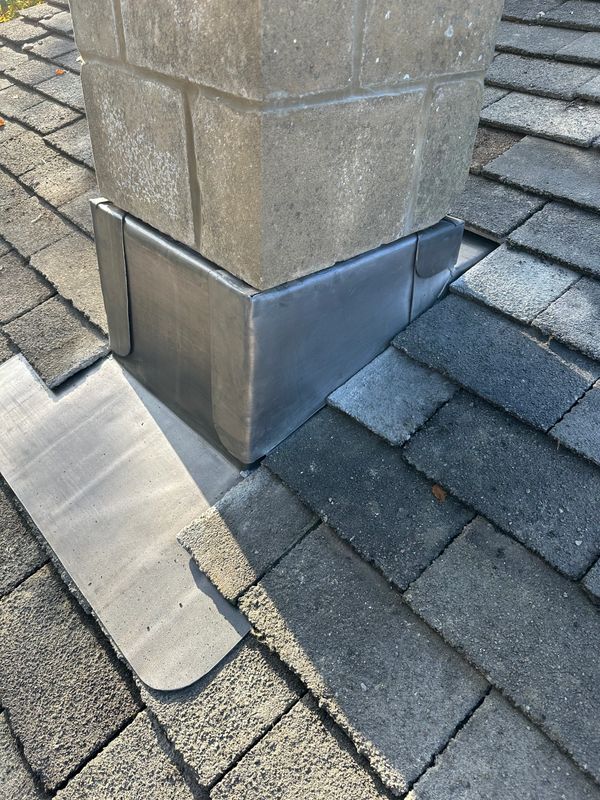 Metal flashing installed around a chimney base on a roof.