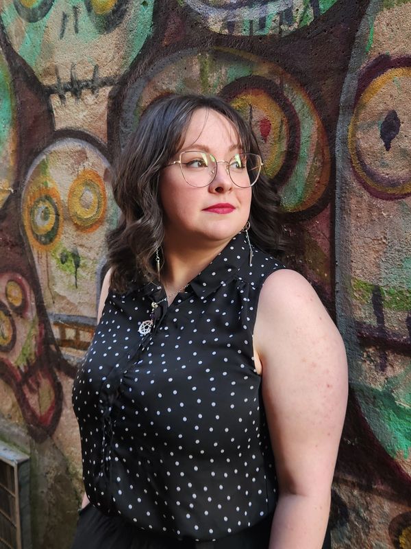 Woman in glasses stands against colorful graffiti wall with skull designs.
