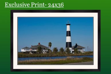 Black and white lighthouse by the water with houses under a clear blue sky.