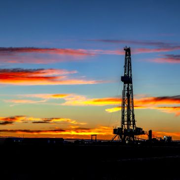 Oil drilling rig silhouetted against a colorful sunset sky.
