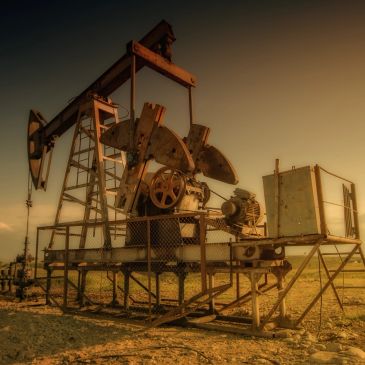An oil pumpjack operating in a dry, open field at sunset.