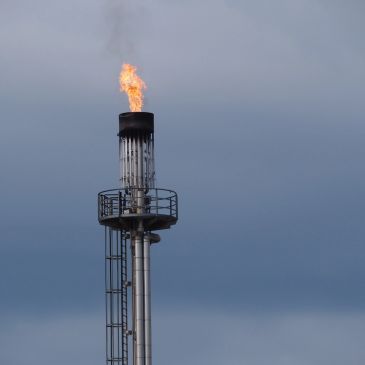 Industrial flare stack burning off excess gas against a cloudy sky.