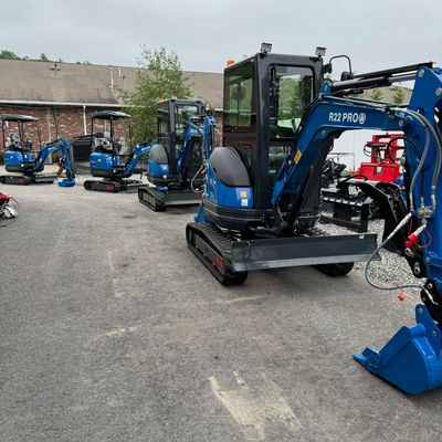 A row of blue mini excavators lined up outdoors on asphalt.