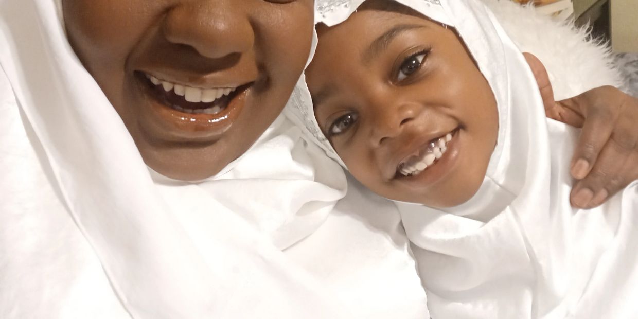 Smiling mother and daughter in white hijabs sharing a happy moment.