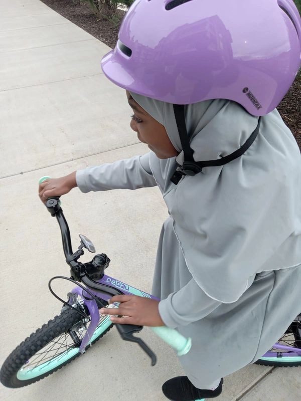 A young girl wearing a purple helmet rides a bike on a sidewalk.