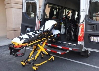 A yellow stretcher outside an ambulance with a wheelchair inside the vehicle.