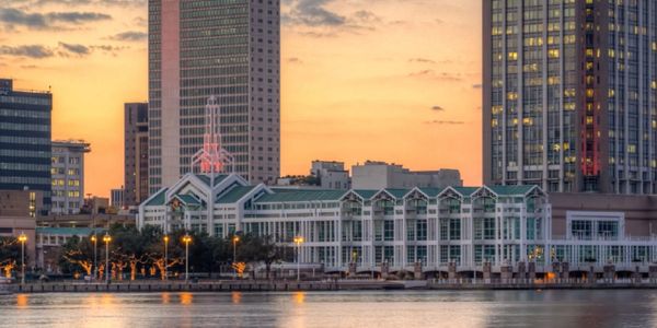 City skyline at sunset with illuminated buildings by the waterfront.
