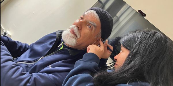 A young woman adjusts an elder man's ear accessory indoors.