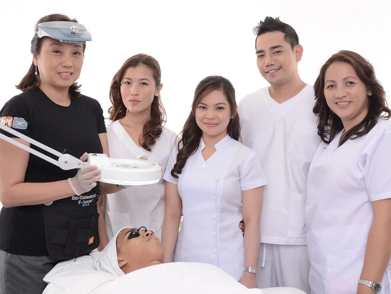 A skincare team with a patient undergoing treatment under a magnifying lamp.