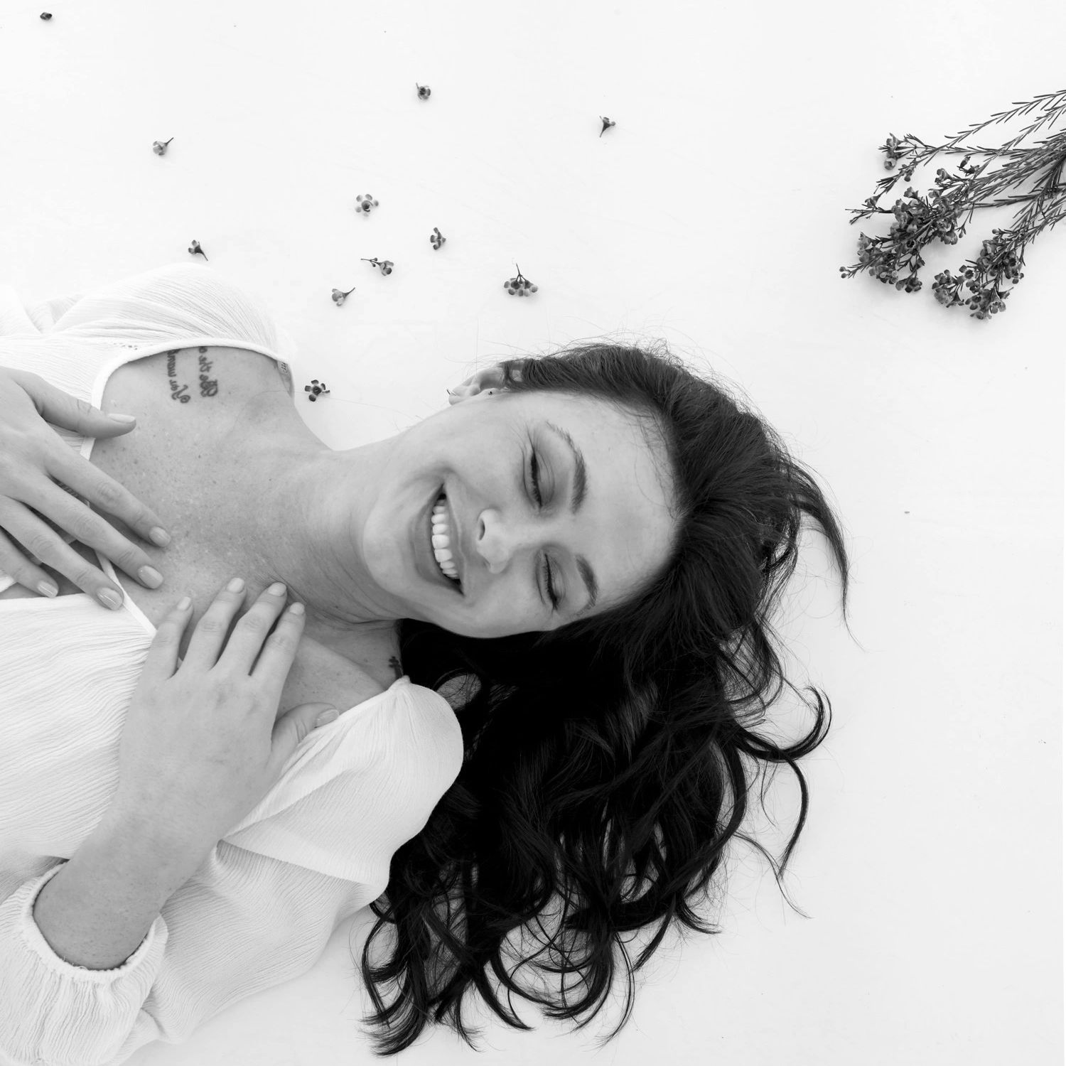 Smiling woman lying down with flowers and flowing hair in a black-and-white photo.