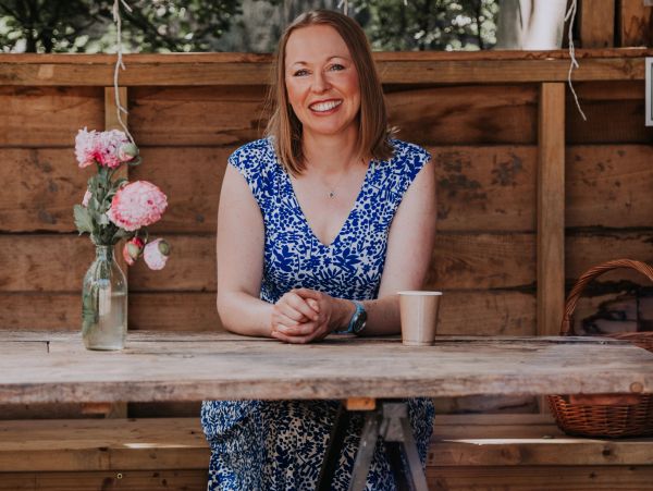 Smiling woman in a blue dress sitting at a wooden table.