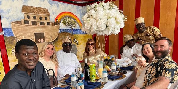 A diverse group enjoying a meal at a decorated table with a colorful mural and floral centerpiece.