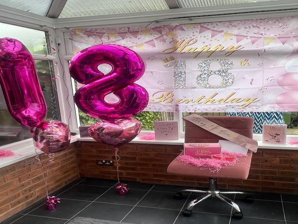 Pink-themed decorations celebrate an 18th birthday with balloons and a sash.