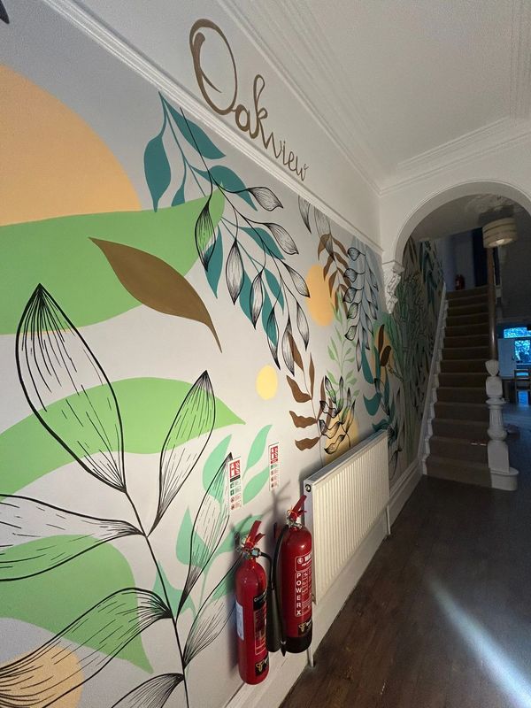Colorful leafy mural with fire extinguishers in a hallway labeled Oakview.