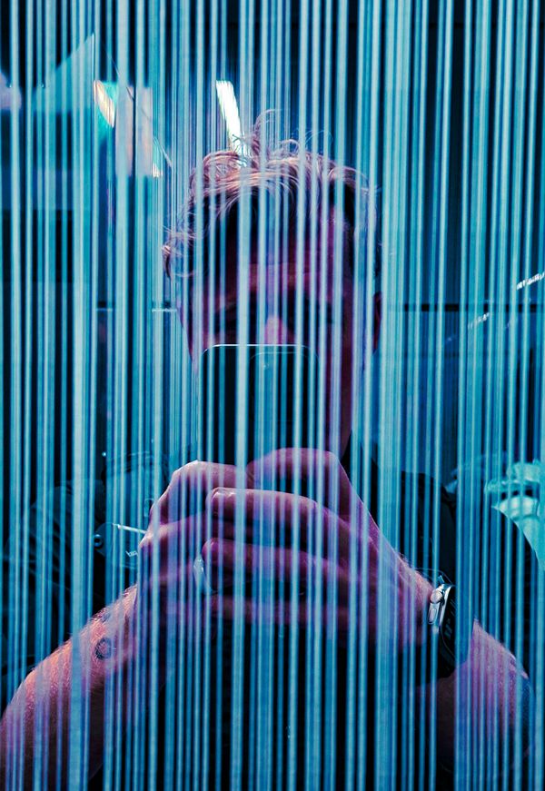 Man taking a selfie behind vertical blue light streaks.