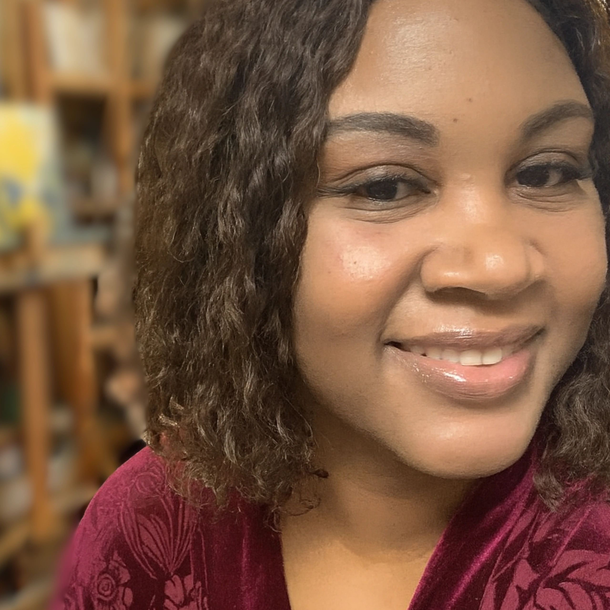 Close-up of a smiling woman with curly hair in a maroon top.
