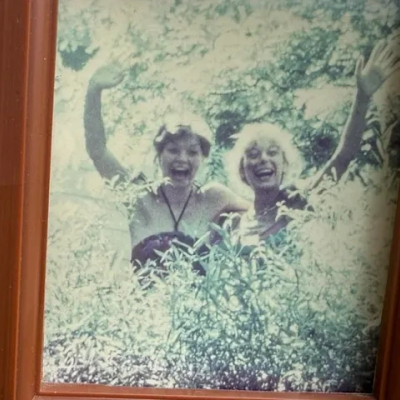 Two women happily posing in a bush with raised arms.