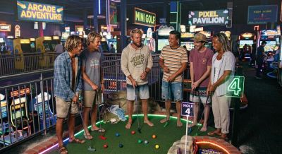 Group of friends playing mini golf indoors at night.