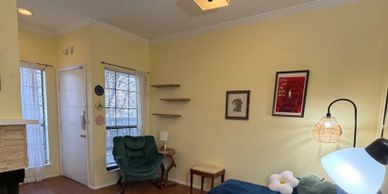 Cozy living room corner with green chair, wall shelves, and soft lighting.