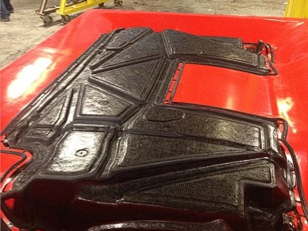 Black textured car hood insulation on a red surface in a workshop.