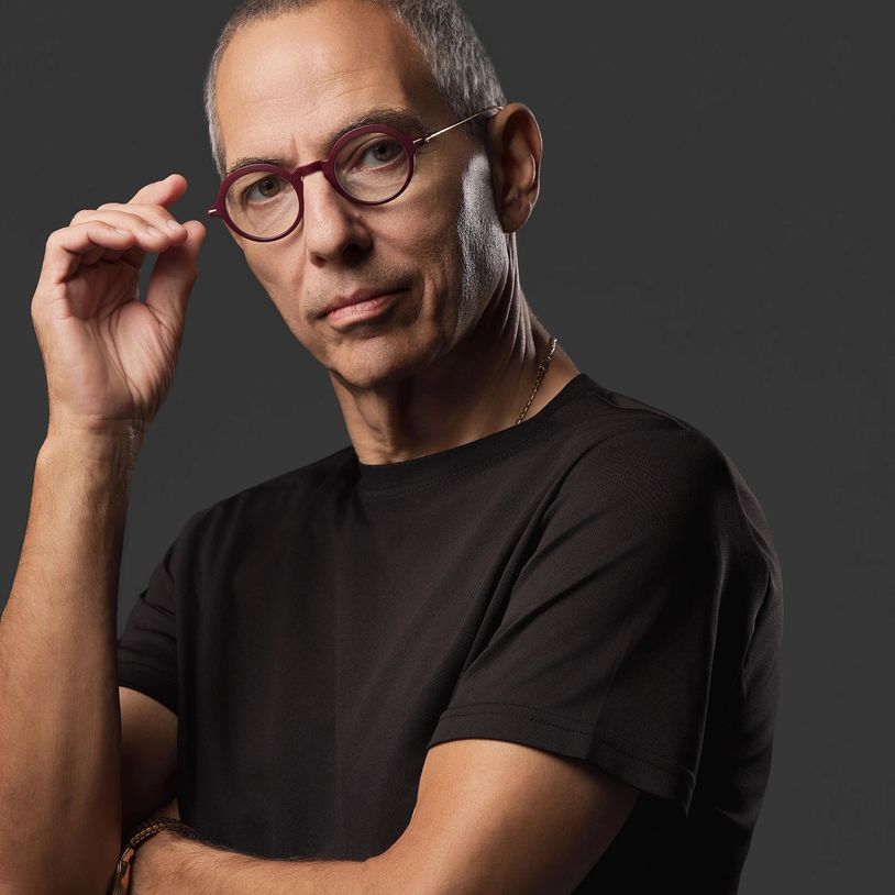 Confident man in round glasses and black shirt poses against a dark background.