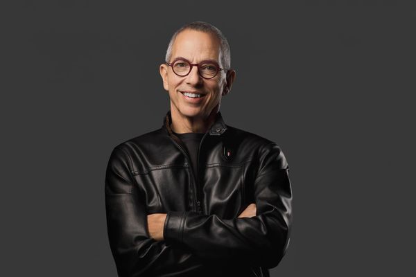 Smiling man in glasses and black leather jacket against dark background.
