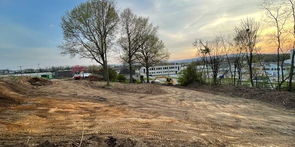 Cleared land with tire tracks and a few trees at sunset near industrial buildings.