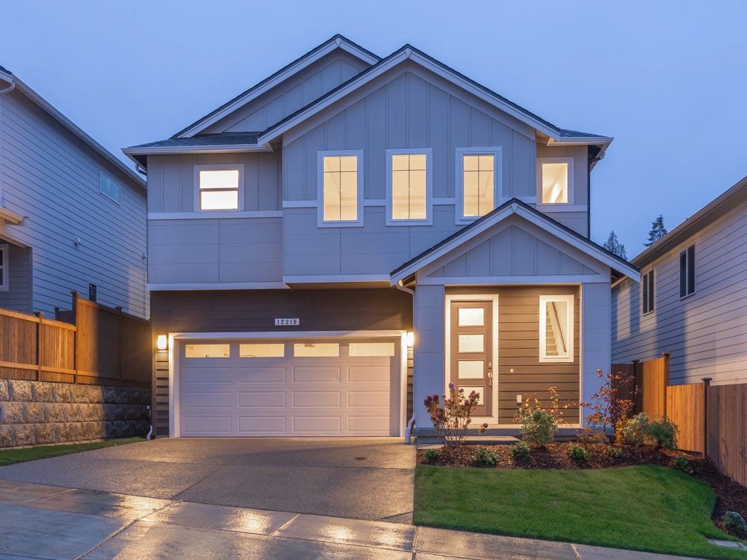 Modern two-story house with illuminated windows and a neatly maintained front yard.