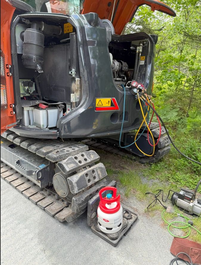 Excavator undergoing maintenance with gauges and refrigerant canister.