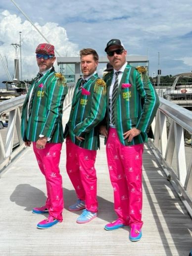 Three men in matching colorful outfits pose on a dock.