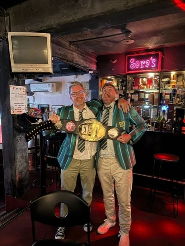 Two men wearing matching striped blazers holding a championship belt.
